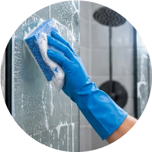 Gloved hand scrubbing hard water spots off a shower door